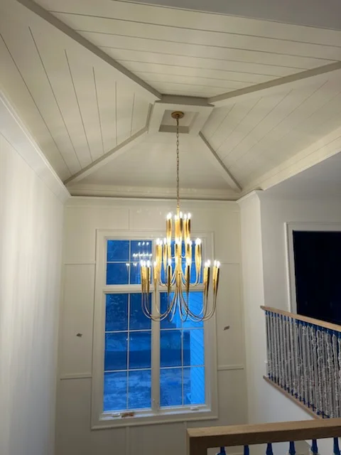Brass multi-tier chandelier installed in white foyer with vaulted shiplap ceiling and tall windows