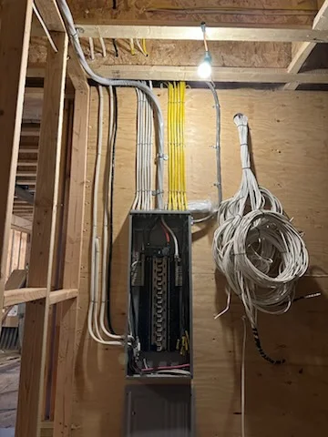 Electrical panel with organized yellow and white THHN wiring, conduit runs, and cable bundles during residential installation