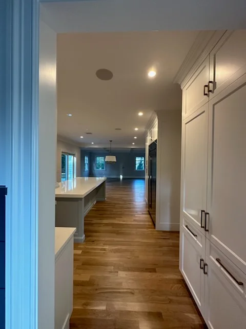 Recessed ceiling lights and pendant fixtures in kitchen with white cabinetry and wood flooring